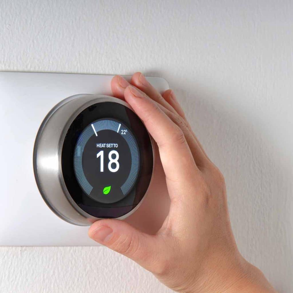 AC mistake #2: Hand adjusting a Google Nest smart thermostat to a very low setting of 18, illustrating the error of setting thermostats too low.