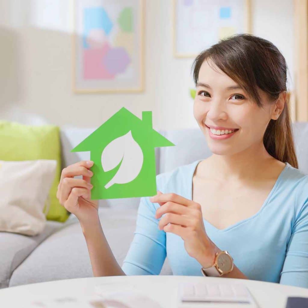 Enhanced energy efficiency means lower bills: Woman happily displays a green house icon, symbolizing savings from AC services by Richard's AC & Appliance Repair.